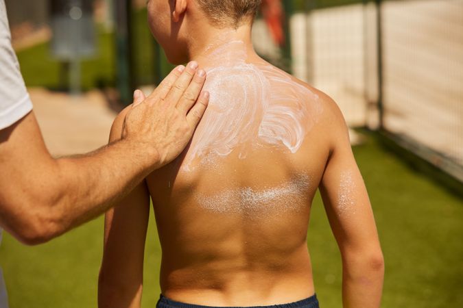 Faceless man applying sun cream on kid