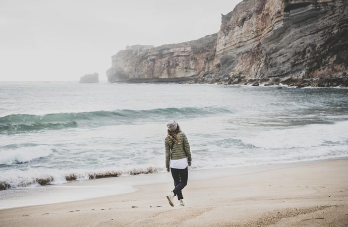 Woman walking on beach in green puffer jacket on fall day