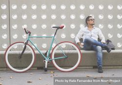 Male looking away while sitting with bike parked in front of patterned cement wall 5l79a0