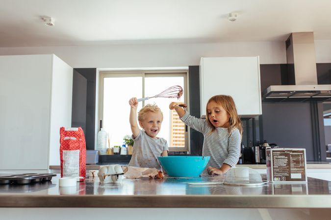 Little boy and girl mixing cake batter in a bowl in kitchen counter