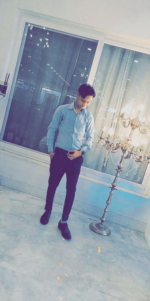 South Asian young man standing beside lamp indoor