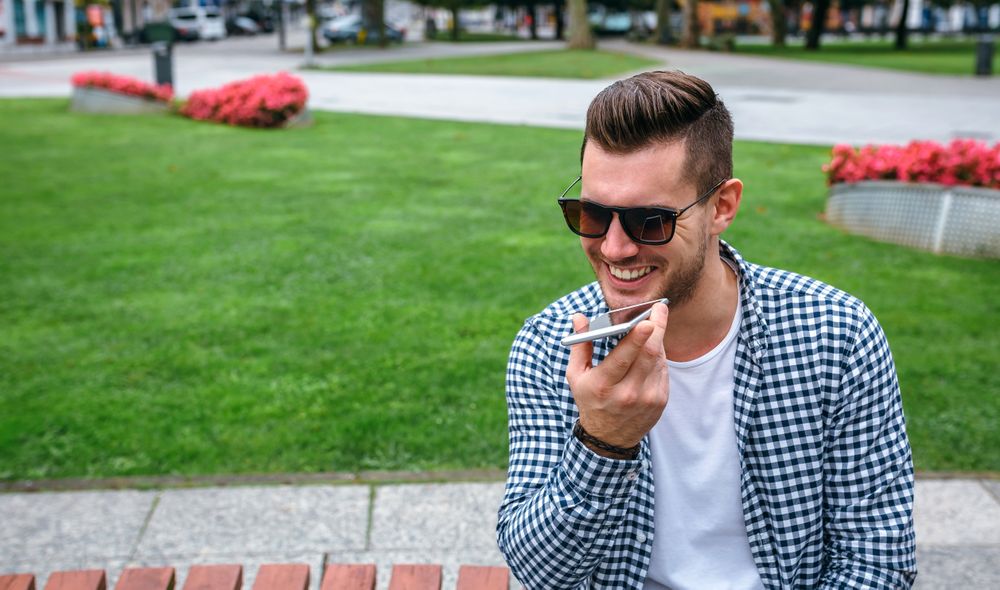 Smiling man sending audio message with mobile