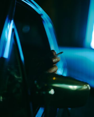 Cropped image of person holding cigarette stick in car at night