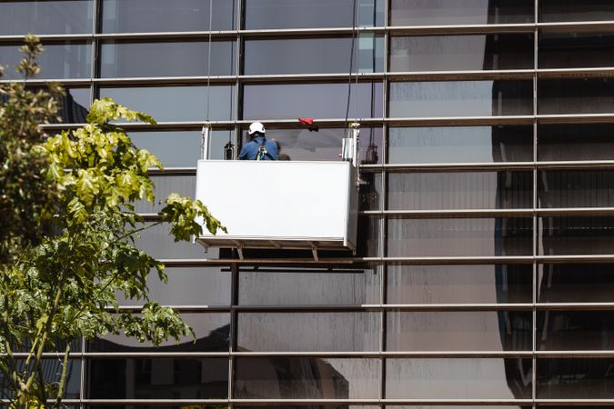 Faceless male window washer cleaning high building facade in construction