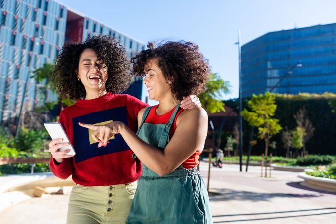 Laughing female couple looking at smartphone together outside