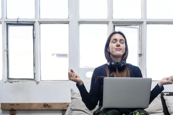 Woman sitting on sofa and meditating in front of laptop