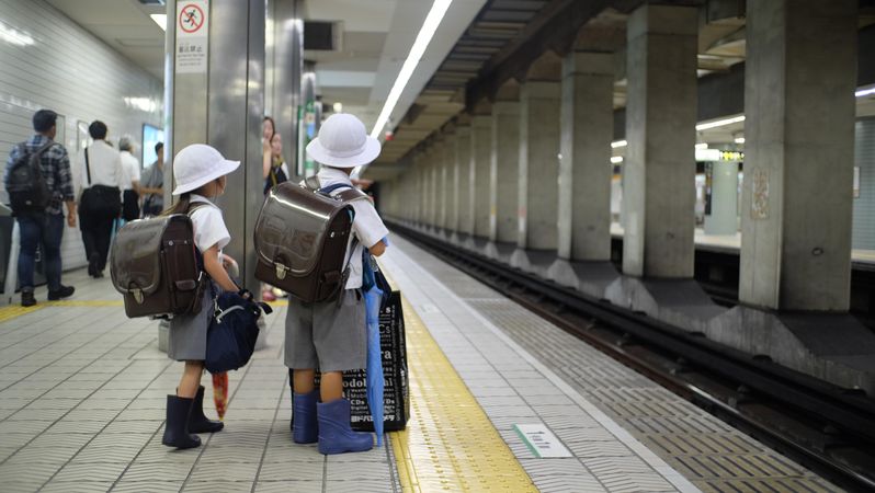 Two children with light hast and backpacks waiting at train station in Japan
