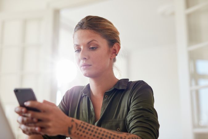 Shot of young woman reading text message on her smart phone while sitting at home