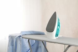 Iron and clean laundry on ironing board, space for text