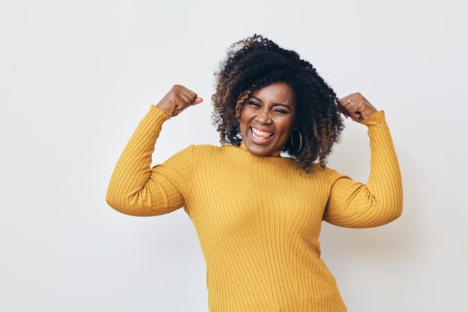 Happy Black woman flexing her arms muscles in a yellow turtleneck