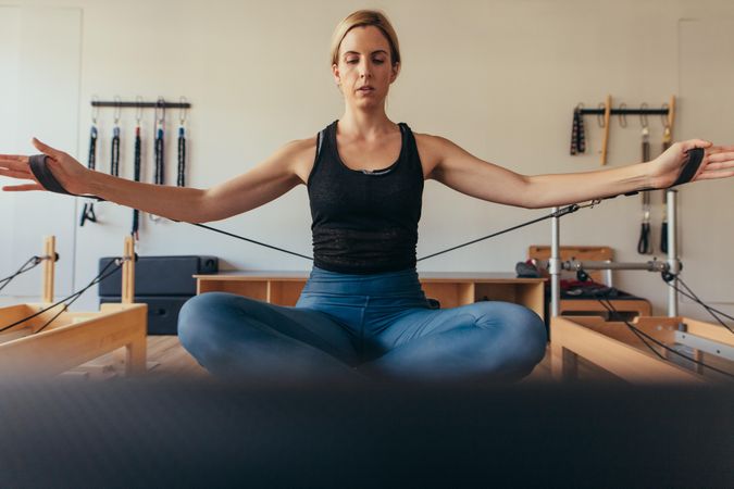 Woman sitting on a pilates training equipment with crossed legs and doing workout