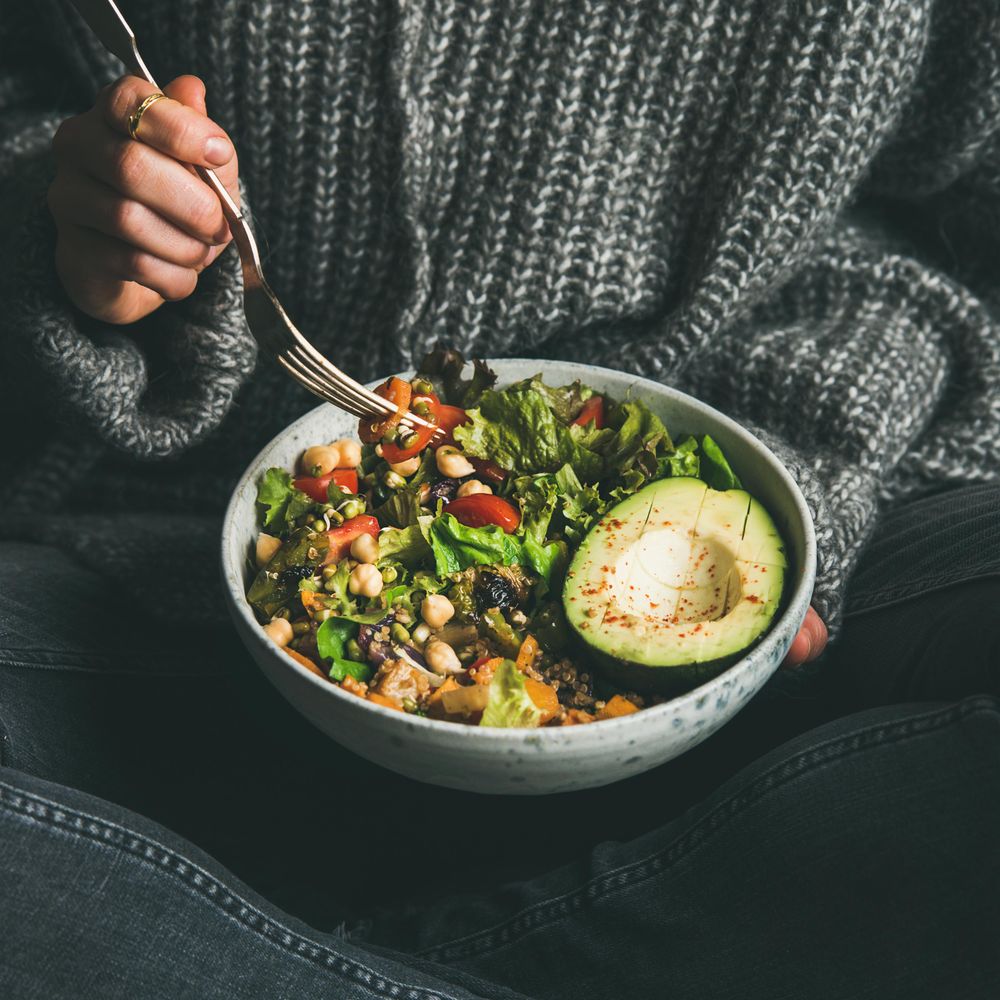Woman in jeans and sweater eating fresh salad, square crop