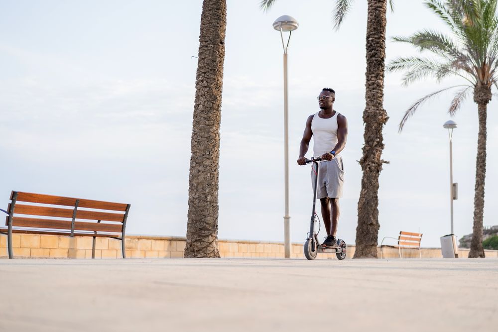 Cool adult Black man riding scooter in street