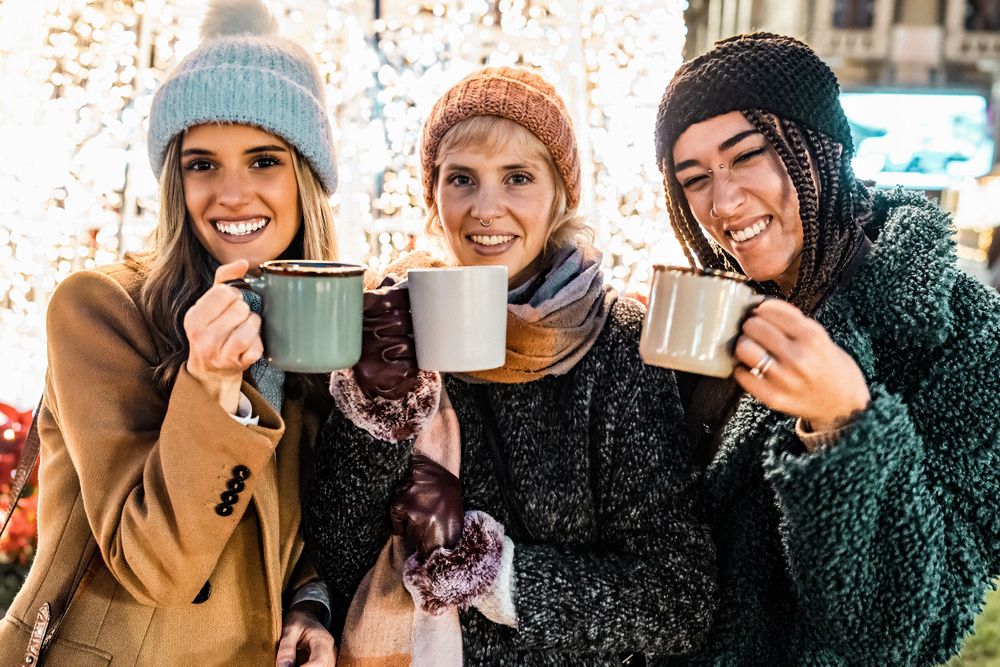 Three happy friends holding mugs and looking at the camera at a Christmas market.