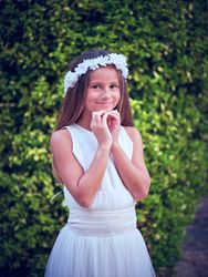Smiling girl in flower wreath standing against green trees