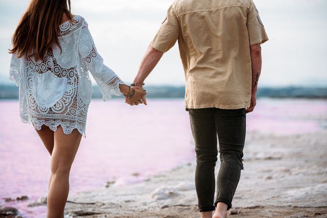 back view of adorable couple walking on an amazing beach with pink water