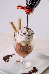 Vanilla and chocolate ice cream served in a glass and topped with chocolate syrup and waffles
