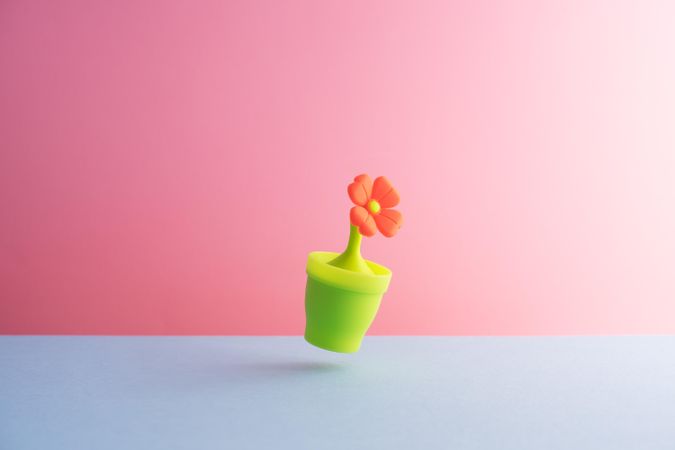 Plastic flower in pot over blue and pink background