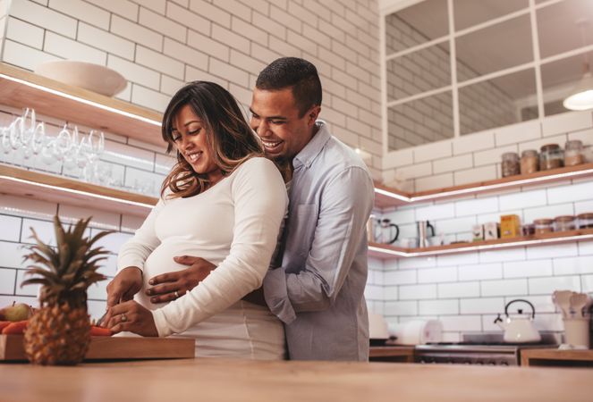 Young couple cooking together in kitchen while man embracing his pregnant wife