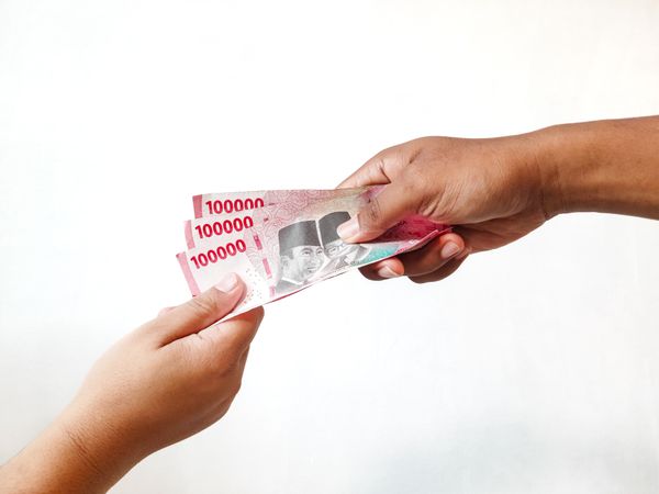 A man's hand gives Indonesian Rupiah banknotes to a woman's hand