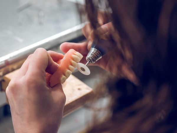 Crop dental technician polishing artificial jaw