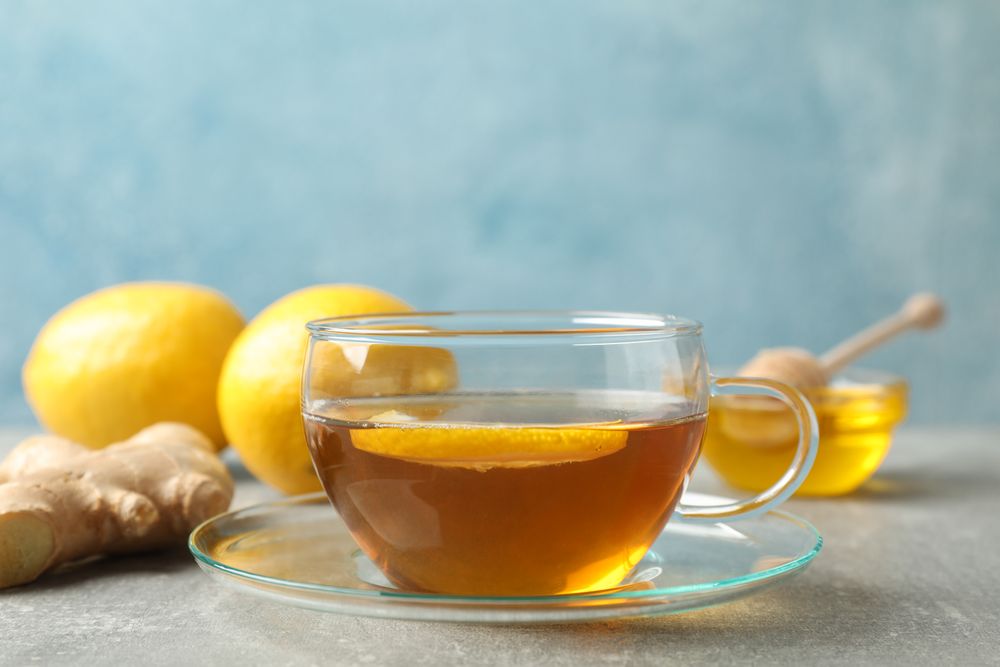 Cup of tea, lemon, honey and ginger on grey background, space for text