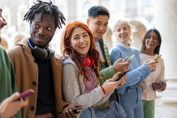 Happy multi-ethnic students standing around campus laughing and checking their phones