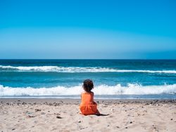 Little girl sitting on beach and admiring view