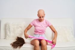 a woman with cancer has taken off her wig and is wearing a pink scarf