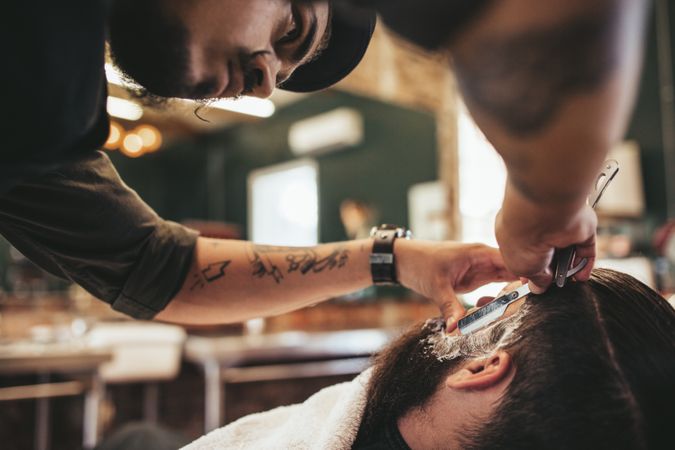 Barber shaving customer’s facial hair with razor