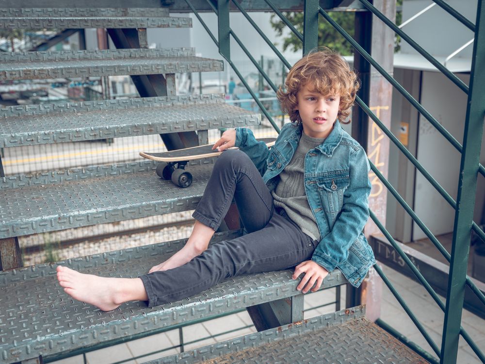 Preteen boy sitting on steps of staircase with skateboard