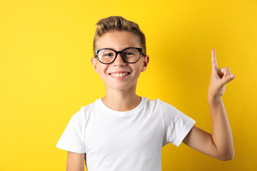 Happy boy in glasses against yellow background, space for text