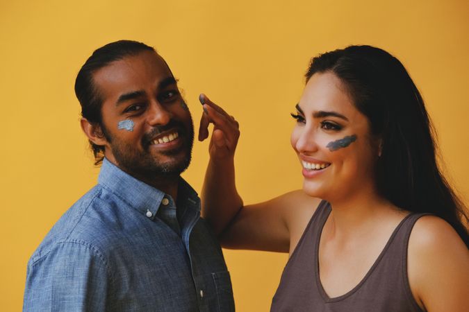 Woman joking and putting beauty mask on male friend