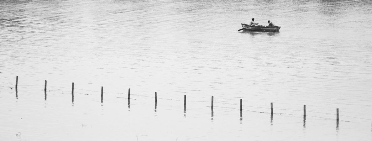 Grayscale photo of two people on boat near piers in Jabalpur, India