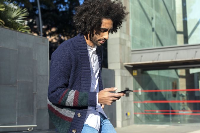 Young Black man using his smartphone while leaning outside on sunny day