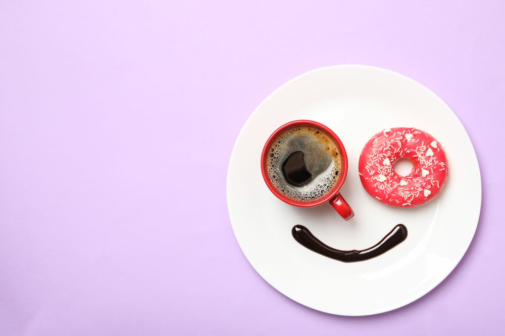 Smile face made of plate with donut, chocolate sauce and coffee on violet background