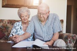 Mature man and woman sitting on sofa and signing some paperwork 56Bvl5