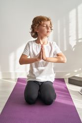 Preteen boy meditating on yoga mat with hands in Namaste