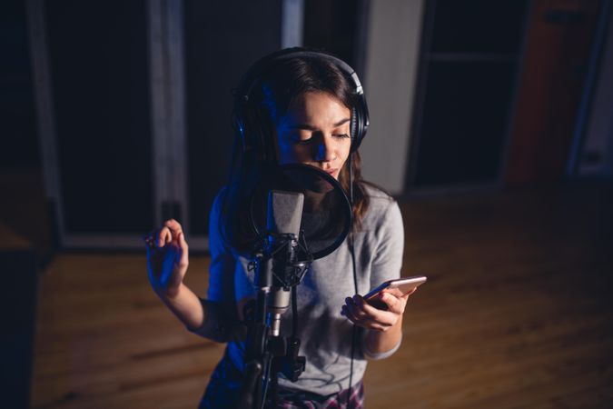 Young woman singing song with microphone and reading lyrics from mobile phon