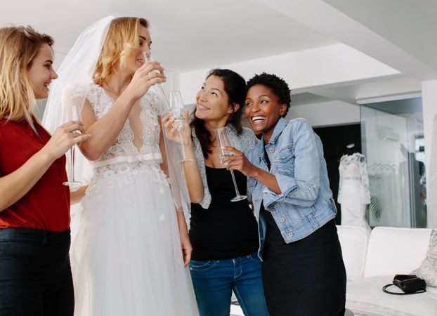 Woman in wedding gown drinking champagne with friends in bridal boutique