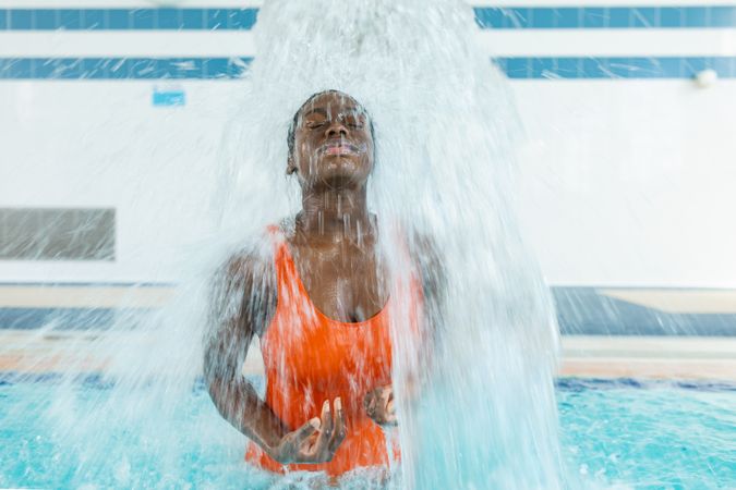 Black young woman massaging her back under a water jet at the swimming pool