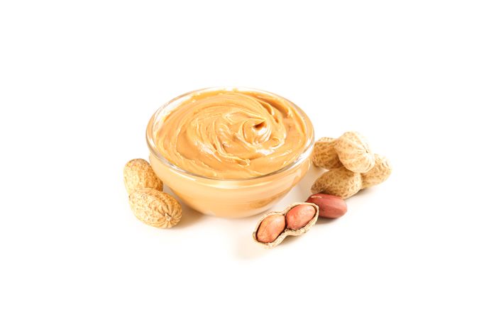 Creamy peanut butter in glass bowl and peanut isolated on light background. A traditional product of American cuisine