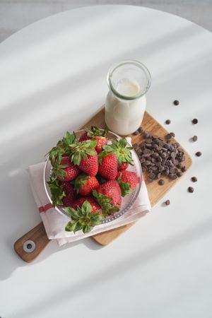Delicious strawberries in bowl and milk in glass bottle on wooden