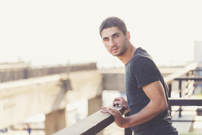 Male standing next to handrails on top of building looking at camera