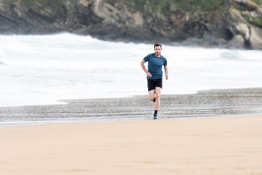 Sportsman in active wear jogging on lonely beach