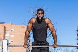 Strong Black sportsman working out on bar in town