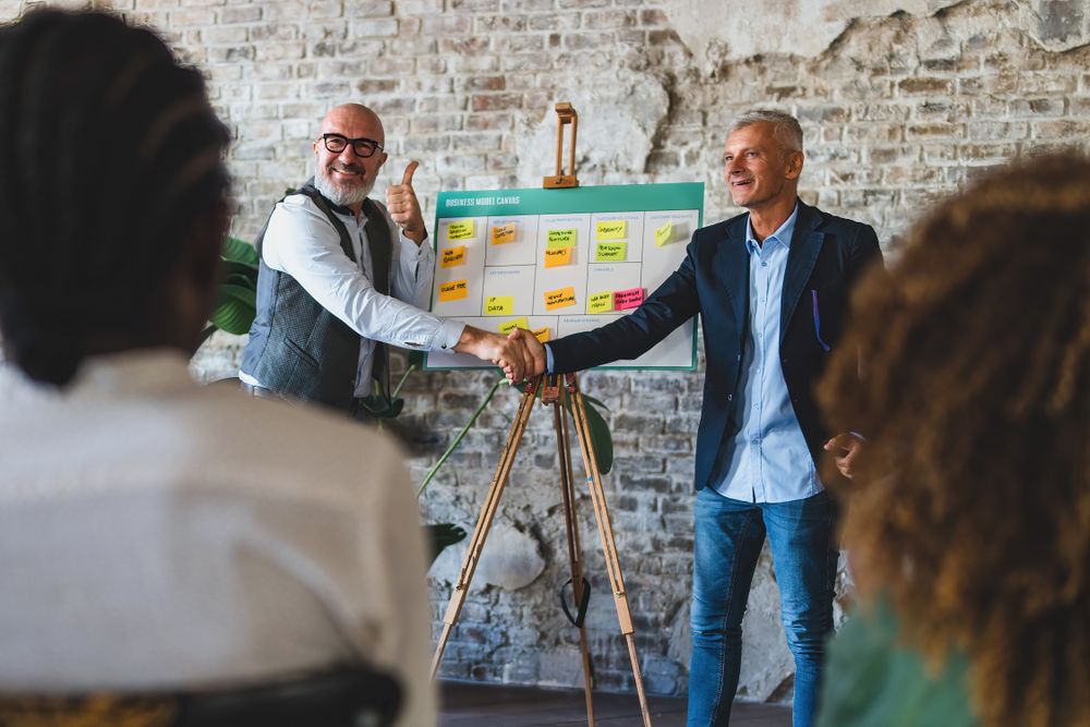 Two mature businessmen shaking hands in front of an audience
