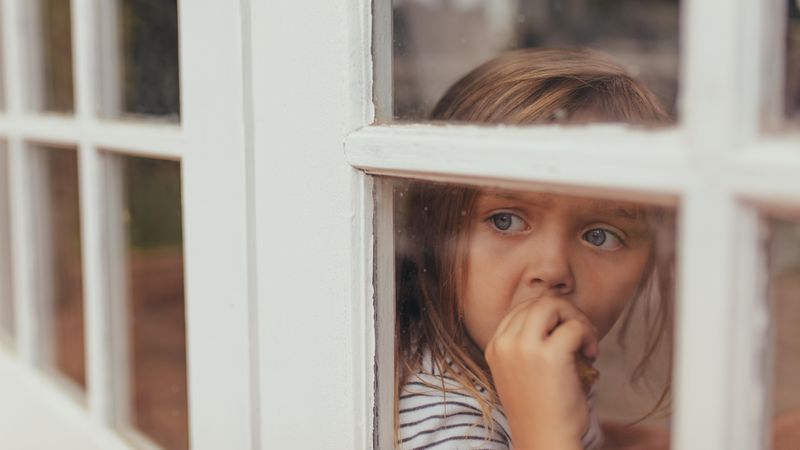 Grey eyed girl eating a cake while looking out of a window