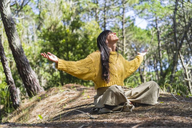 Woman sitting on the woods with arms opened while looking to the sky like thanking God