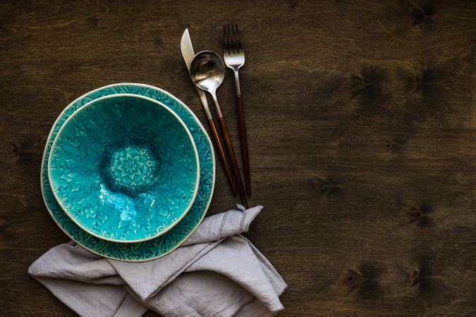 Rustic table setting of patterned teal bowl with cutlery with copy space
